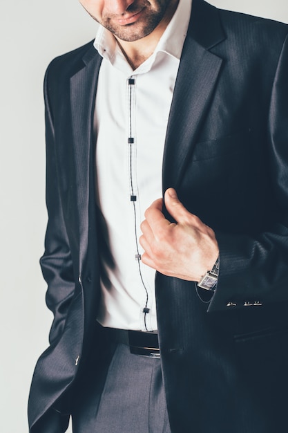 Man in a luxurious classic suit poses on a photo session. He holds a black jacket with his fingers