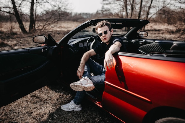 man in a luxury car a red convertible sits in nature a rich life