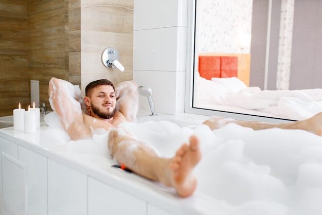 Uomo disteso nella vasca da bagno con schiuma al mattino.