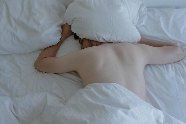 Foto uomo sdraiato sul letto a faccia in giù con un cuscino sopra la testa