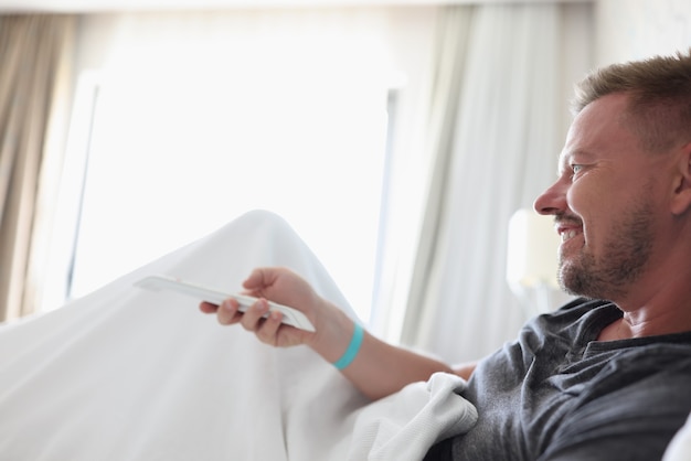 Man lying in bed and holding tv remote control at home