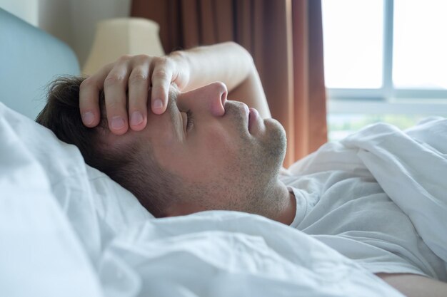 Man lying in bed at home suffering from headache or hangover