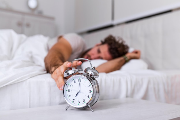 Man lying in bed turning off an alarm clock in the morning at 7am. Hand turns off the alarm clock waking up at morning, man turns off the alarm clock waking up in the morning from a call.