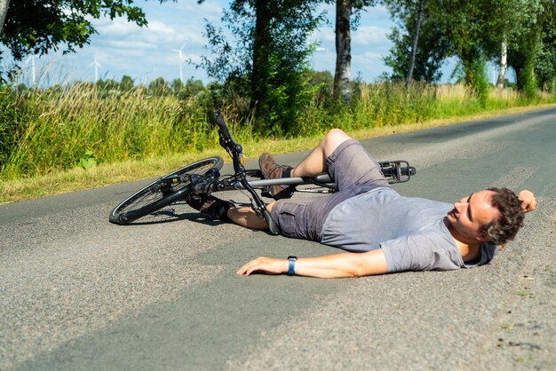 Man lying by bicycle on road against sky