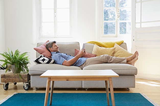 Man lying on couch at home, using digital tablet