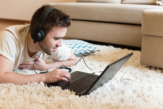 Man lying on the floor using headphones on laptop