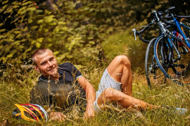 Man lying on grass in the forest. Two bicycles on background.