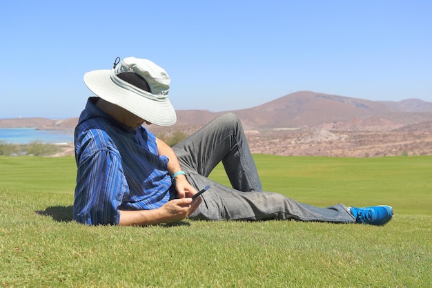 A man lying in the grass, relaxes while looking at his mobile phone