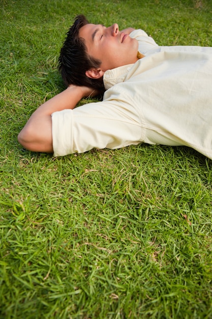 Man lying in grass with his eyes closed and both hands behind his head