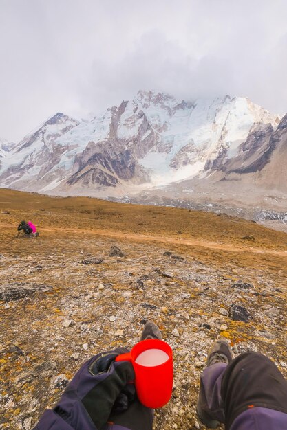 Man lying on a hill with a cup of fresh milk of yakmu female of\
yak animal view of mountains and sky in gorakshep village nepal\
everest base camp trail route nepal trekking