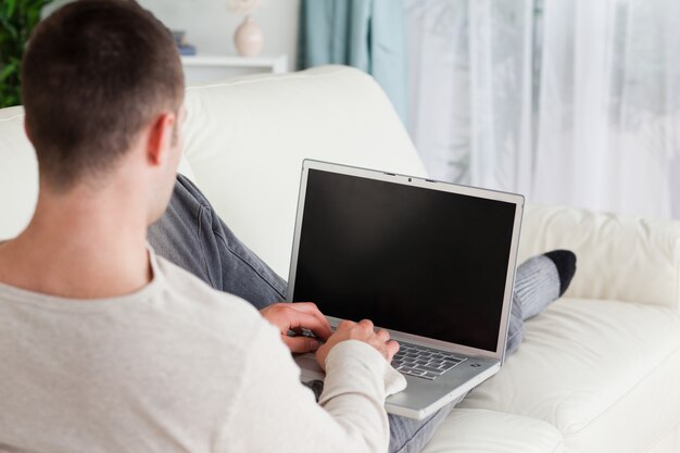 Man lying on his couch to use a laptop