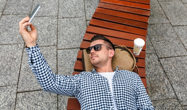 Man lying on a park bench making selfie with mobile