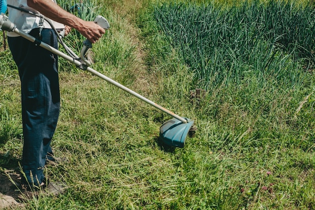 Man maait het gras van het gazon met een grasmaaier. benzine grasmaaier, grastrimmer. De man werkt in de tuin