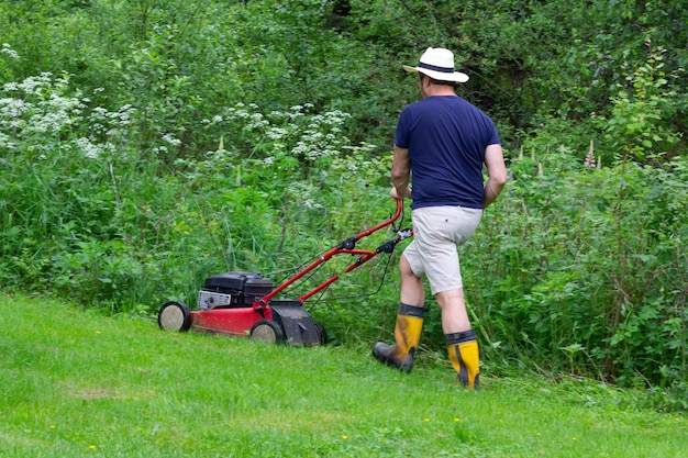 Man maait het groene gazon in zomerpark