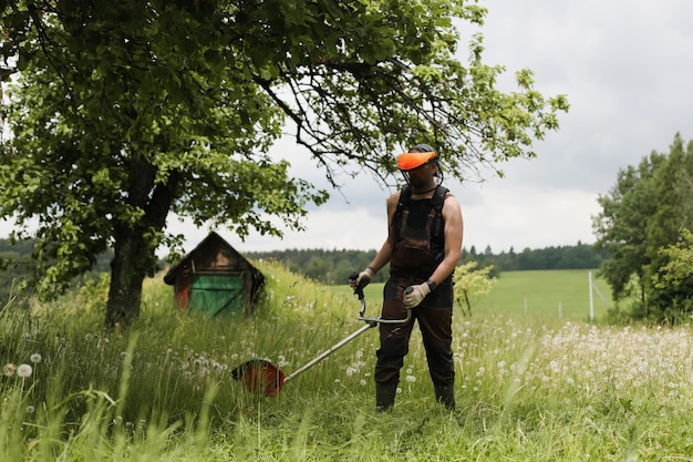 Man maait hoog gras met benzine grastrimmer in de tuin of achtertuin Proces van grasmaaien met handmaaier