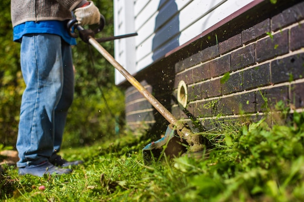 Man maait hoog gras met elektrische of benzine grastrimmer in achtertuin Tuinieren verzorgingshulpmiddelen en apparatuur Proces van gazon trimmen met handmaaier