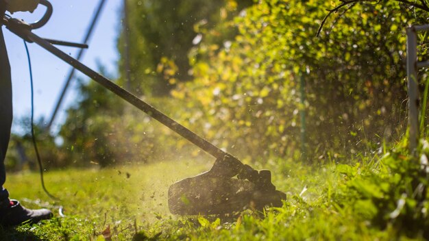 Man maait hoog gras met elektrische of benzine grastrimmer in achtertuin Tuinieren verzorgingshulpmiddelen en apparatuur Proces van gazon trimmen met handmaaier