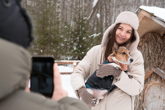 man maakt foto van vrouw met hond die smartphone gebruikt in winterpark