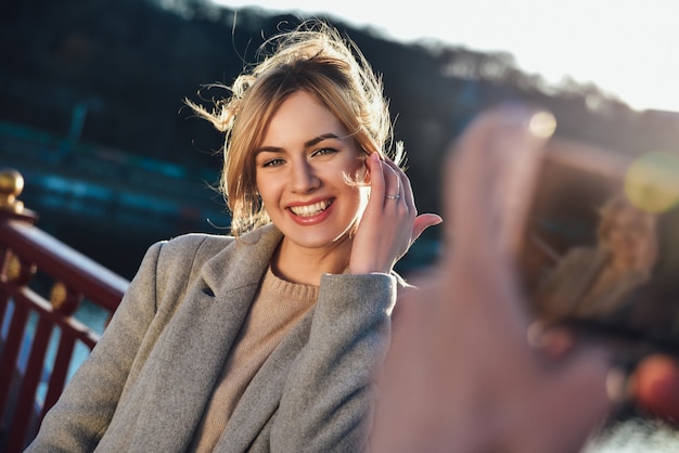 Un uomo fa un ritratto di donna sorridente felice in piedi sul ponte in estate soleggiata o in primavera all'aperto