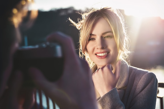 A man make a portrait of happy smiling woman standing on the bridge on sunny summer or spring day outdoor