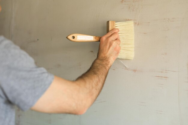 A man makes repairs he covers the walls with glue by a brush\
before wallpapering