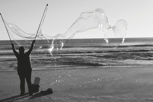Foto uomo che fa grandi bolle sulla spiaggia contro un cielo limpido