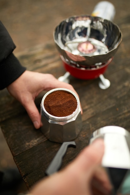 Man making camping coffee outdoor with metal geyser coffee maker on a gas burner, step by step.