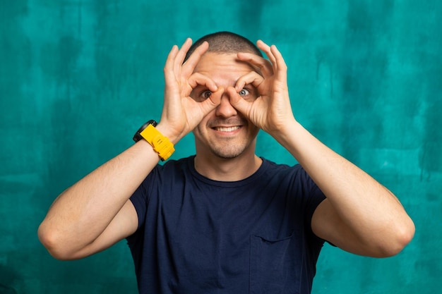 Man making an eyeglasses from his hands and fingers. Funny man at green background.