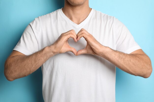 Man making heart with hands on light blue background closeup