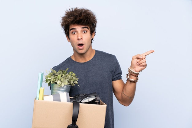 Man making a move while picking up a box full of things surprised and pointing finger to the side