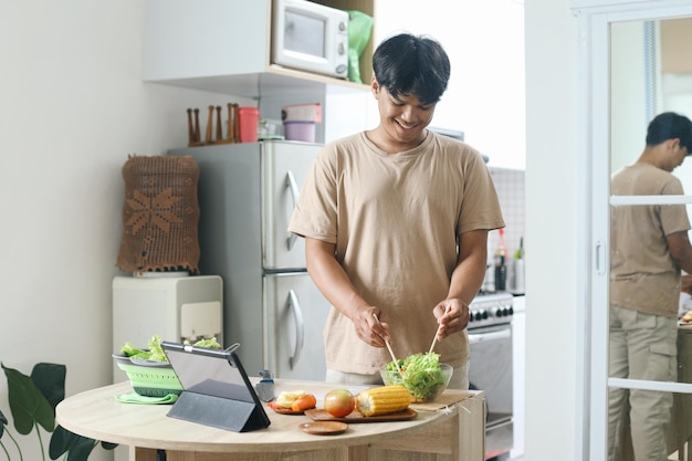 男性がキッチンでタブレットでオンライン料理コースを見ながらサラダを作っています