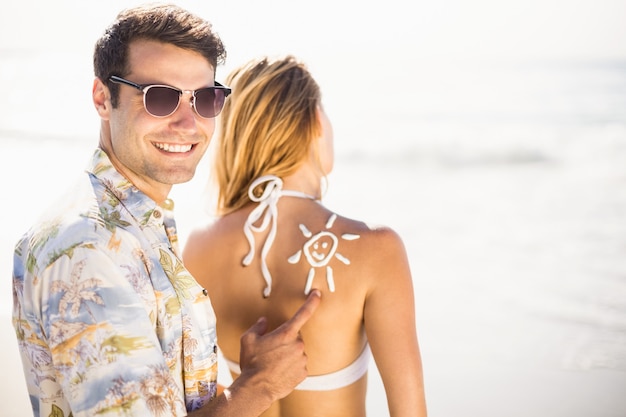 Man making a sun symbol on womans back while applying a sunscreen lotion