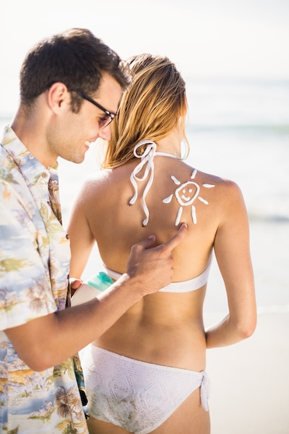 Человек делает символ солнца на спине женщины во время применения солнцезащитный лосьон