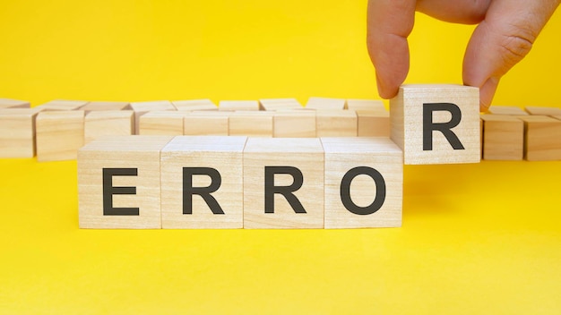 Man making word Error with wooden cubes at yellow table, closeup. Space for text