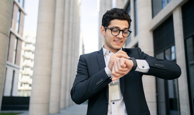안경을 쓴 남자 매니저 사업가가 웃고 있는 스마트워치를 사용하여 사무실에서 일할 예정입니다.