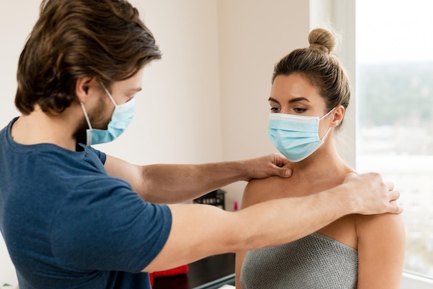 Man manueel therapeut met preventiemasker werkt met een vrouwelijke cliënt in de massagekliniek