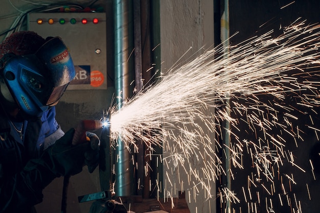 Man in mask cuts metal with plasma cutter. Helmet and spakrs.