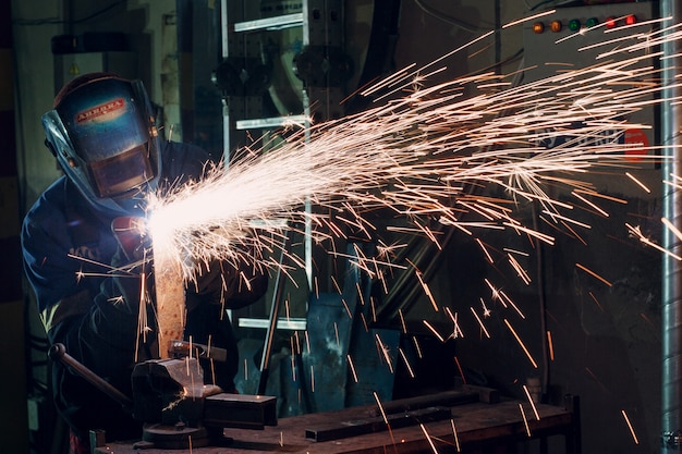 Man in mask cuts metal with plasma cutter. Helmet and spakrs.