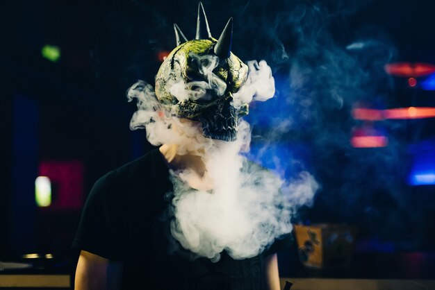 Man in a mask smokes a hookah and lets a cloud of smoke