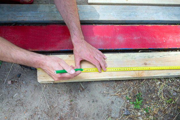 A man measures wooden boards with a construction tape measure closeup