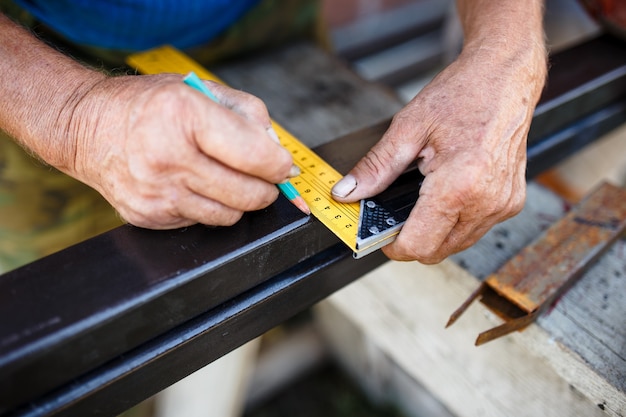 Man measuring off metal bar in workshop.