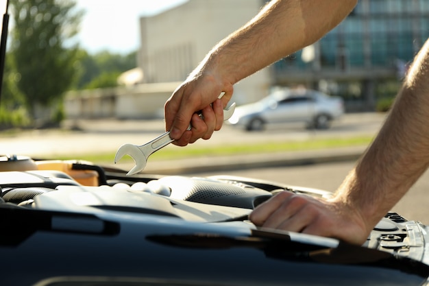 A man mechanic holds a wrench over a car engine