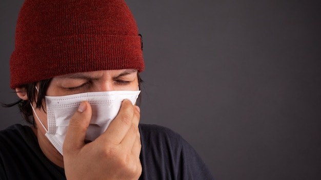 Man in medical disposable mask sneezes because of the flash 2019-nCoV. coronavirus flu quarantine close-up copy space.