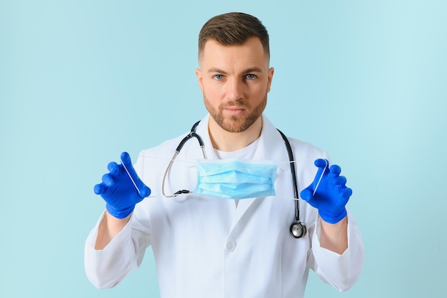 Мужчина в медицинских перчатках надевает защитную маску на синем фоне