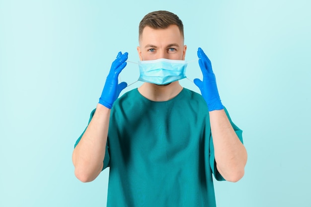 Man in medical gloves putting on protective face mask against blue background