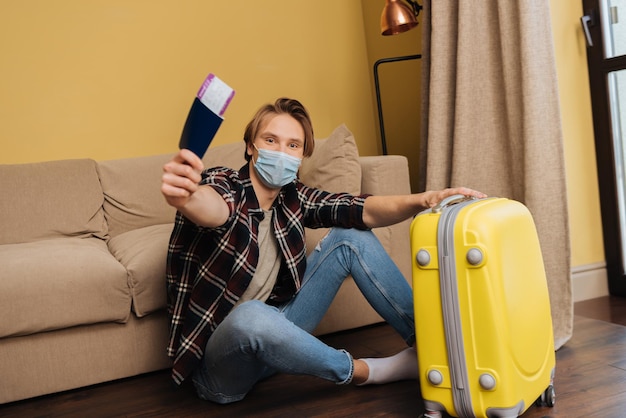 Man in medical mask holding passport with air ticket near baggage end of quarantine concept