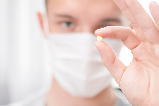 Man in medical mask holding a pill in his hands