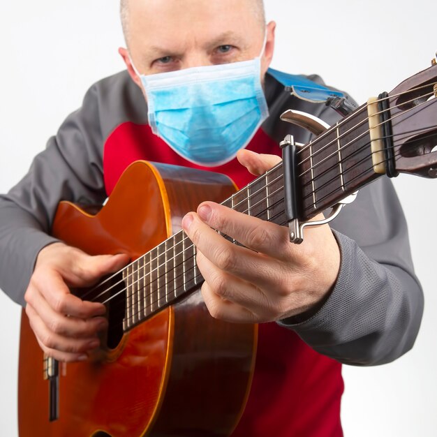 Man in a medical mask plays the classical guitar on a white space. musical creativity. string musical instrument