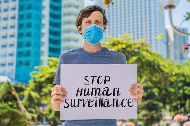 Man in medical mask prevents coronavirus disease holds a poster stop human surveillance hand written