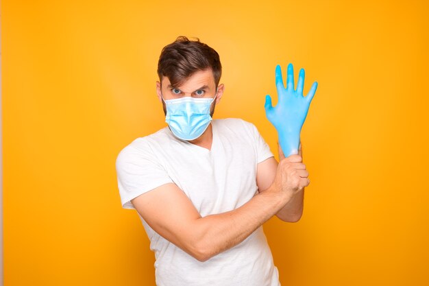 A man in a medical mask puts on sterile blue gloves.